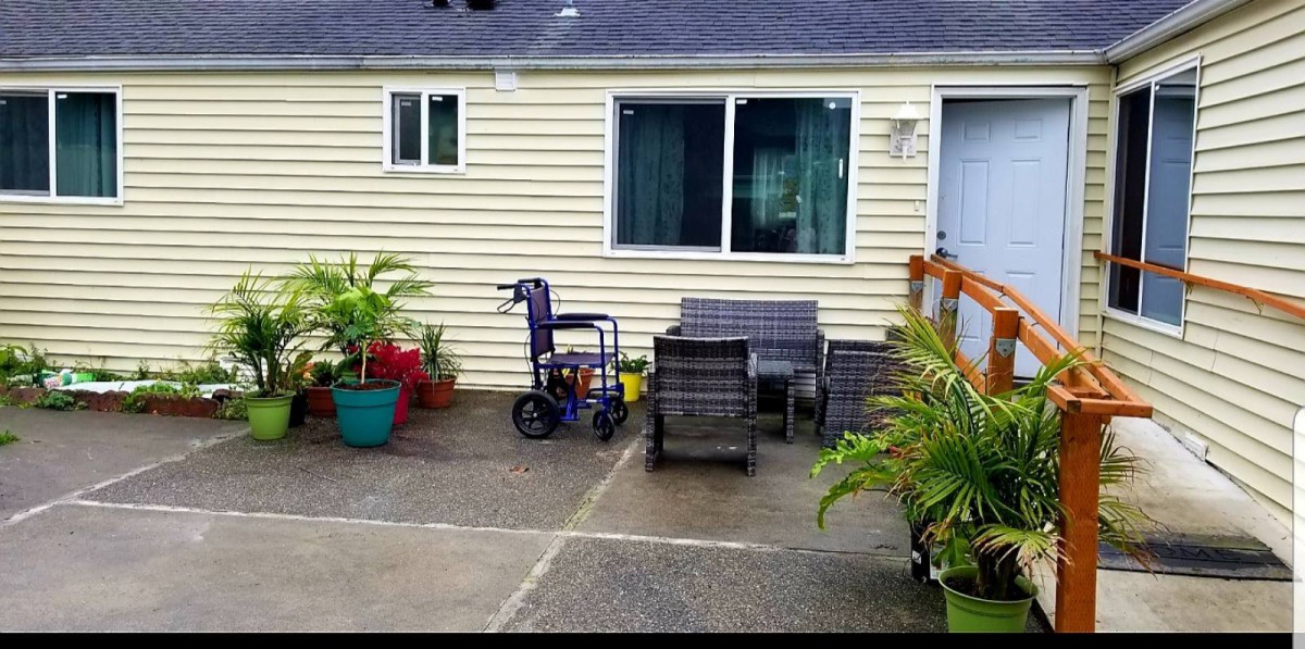 A patio area with outdoor furniture and a wheelchair next to potted plants outside a house.