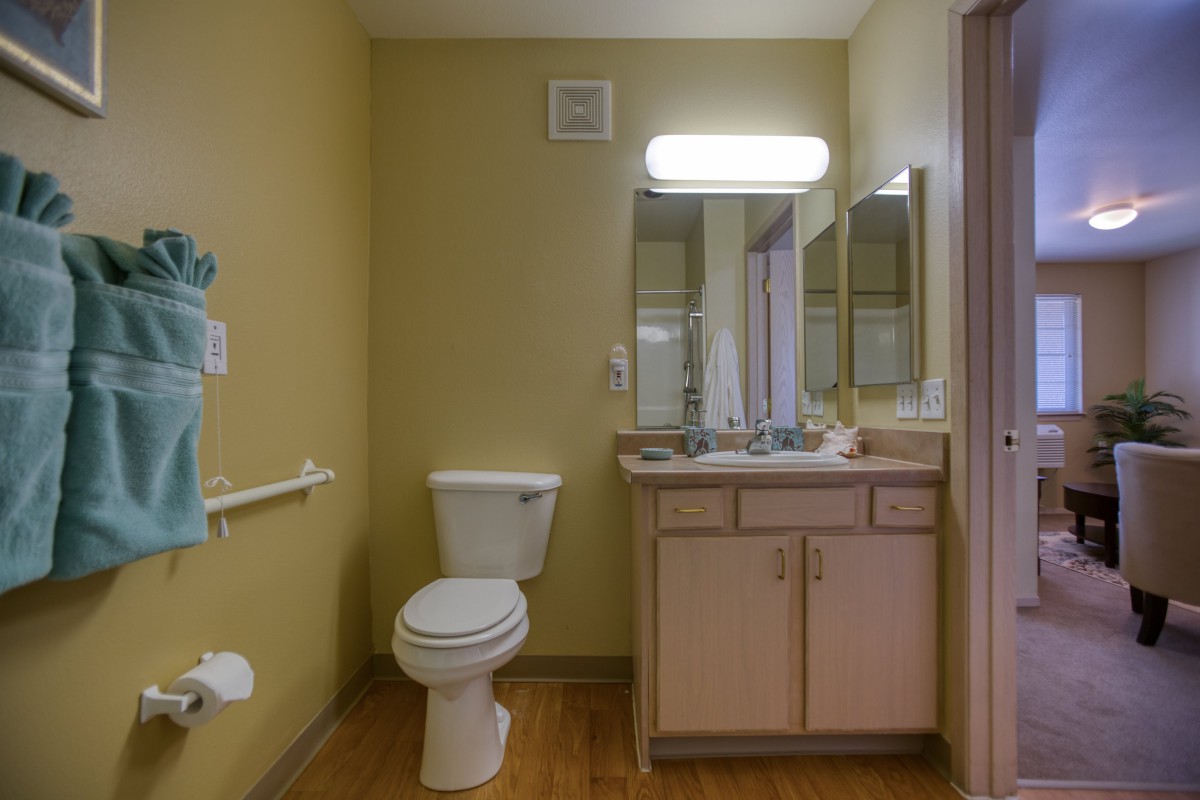 A modest bathroom featuring a toilet, sink with vanity, and a mirror illuminated by a wall-mounted light.