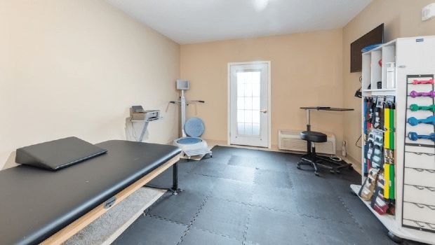 A home gym equipped with various exercise machines and a table in a well-lit room.