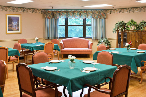 A cozy dining room setup featuring tables with green tablecloths, chairs, and a comfortable sofa by the window.