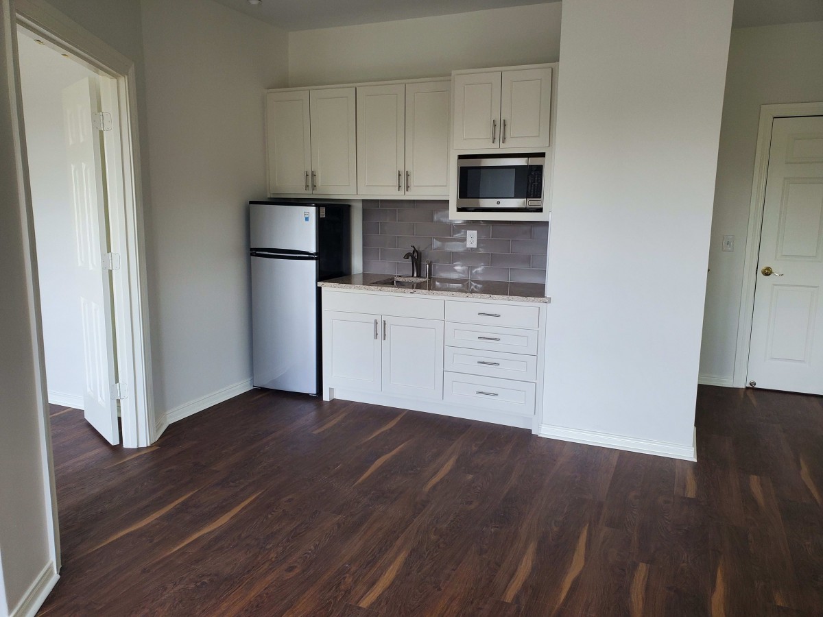A small, modern kitchen in an apartment with wood flooring and white cabinets.