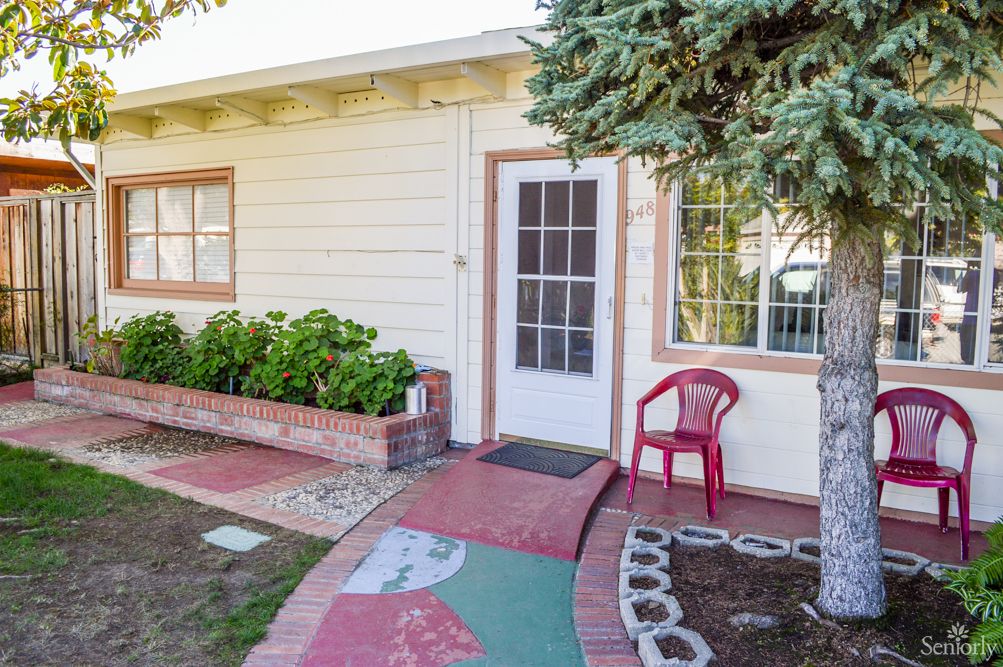 A small house entrance with a pathway, garden, and a red chair.
