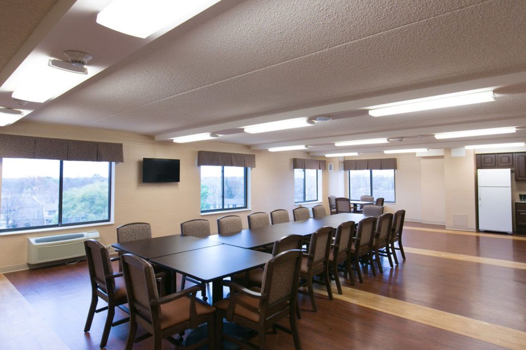 A spacious conference room with a long meeting table surrounded by chairs, featuring large windows and a wall-mounted television.