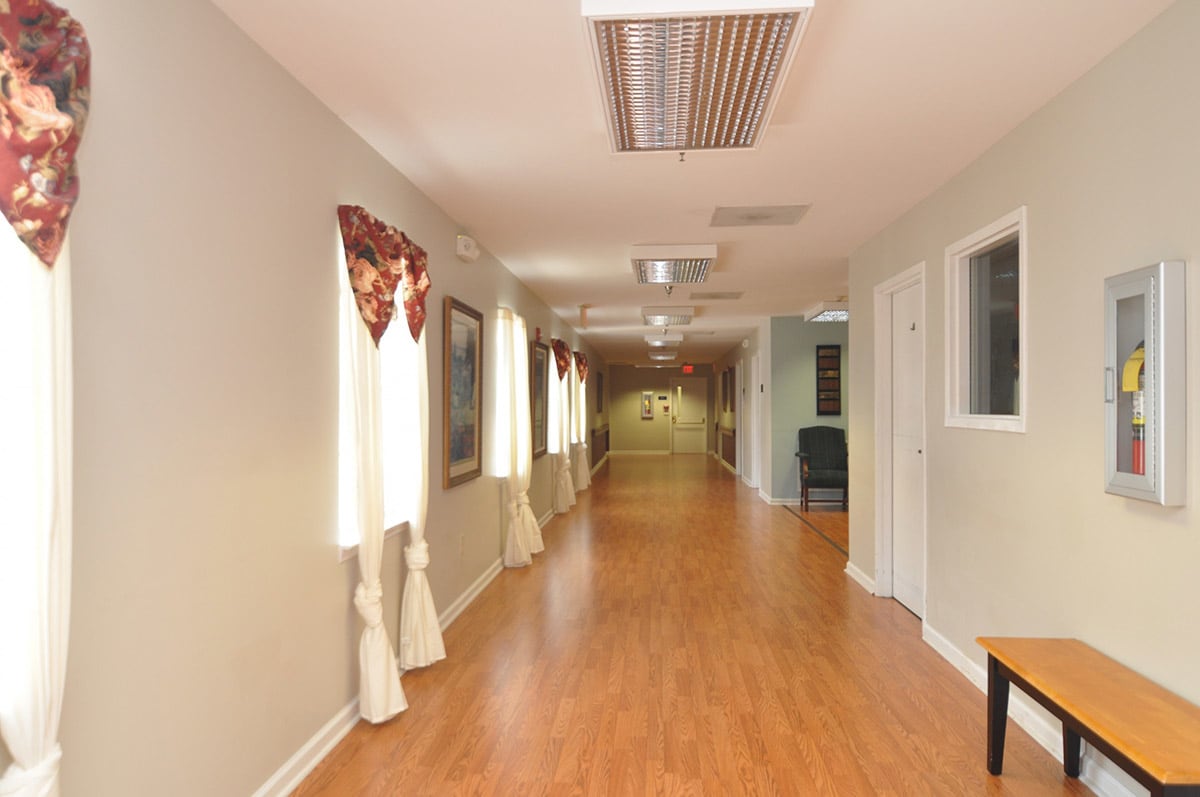 A well-lit hallway with wooden flooring and curtains along the windows.