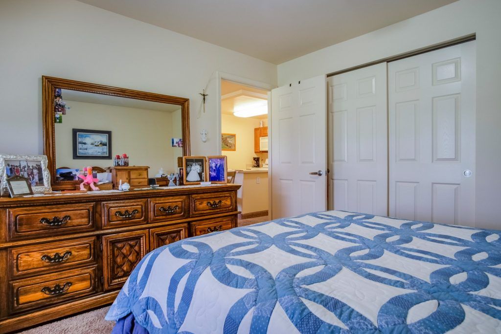 A cozy bedroom featuring a bed with a blue-patterned quilt, a wooden dresser with a mirror, and various decorative items.