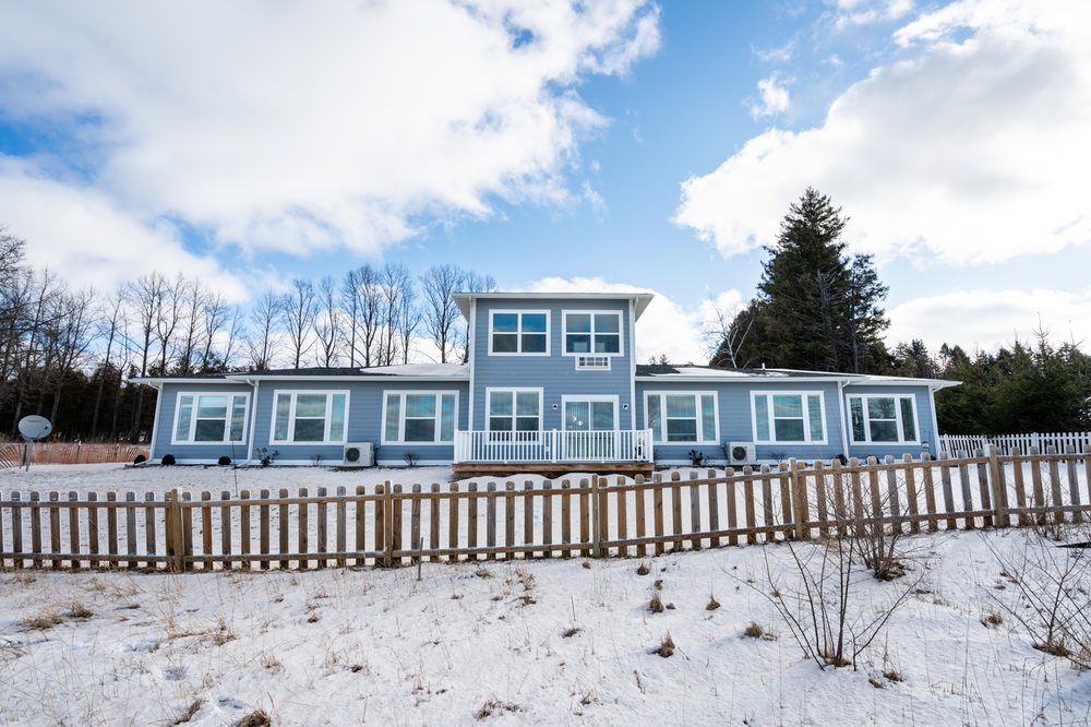 A modern house with a snowy yard and blue skies in the background.