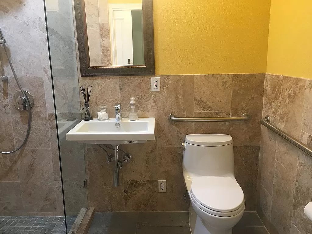 A modern bathroom with a toilet, sink, and mirror, featuring tiled walls and a yellow accent wall.