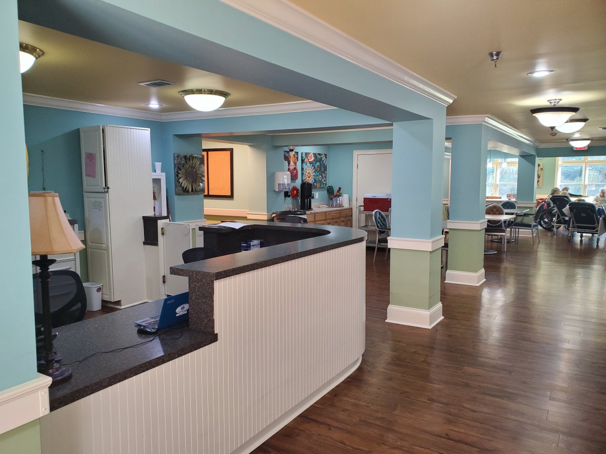 A spacious and welcoming nursing home reception area with light blue walls and wood flooring.