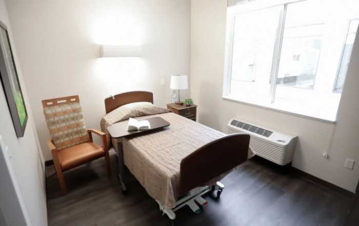 A hospital room with a single bed, chair, and natural light from a window.