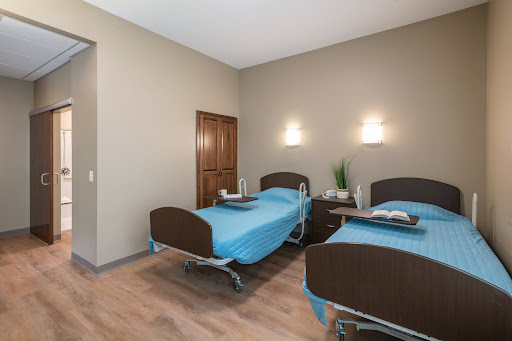 A well-lit hospital room featuring two patient beds with blue bedding.