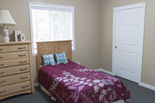 A cozy bedroom featuring a single bed with floral bedding and natural light coming from the window.