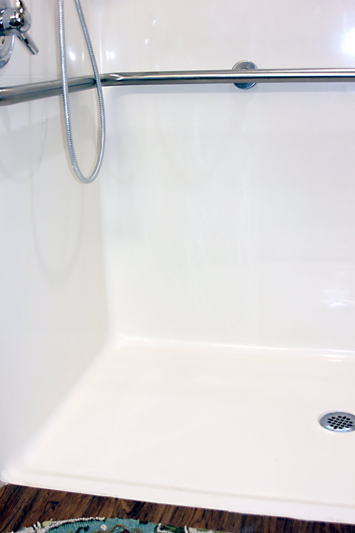 A clean, white shower area with a visible drain and wall-mounted shower head.