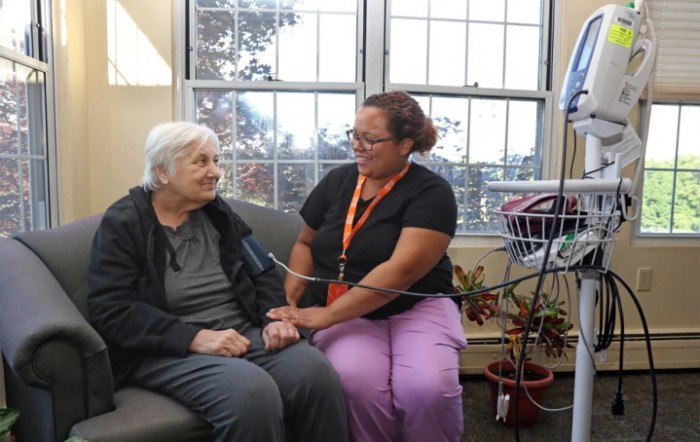 A nurse checks the blood pressure of an elderly patient in a cozy room setting.