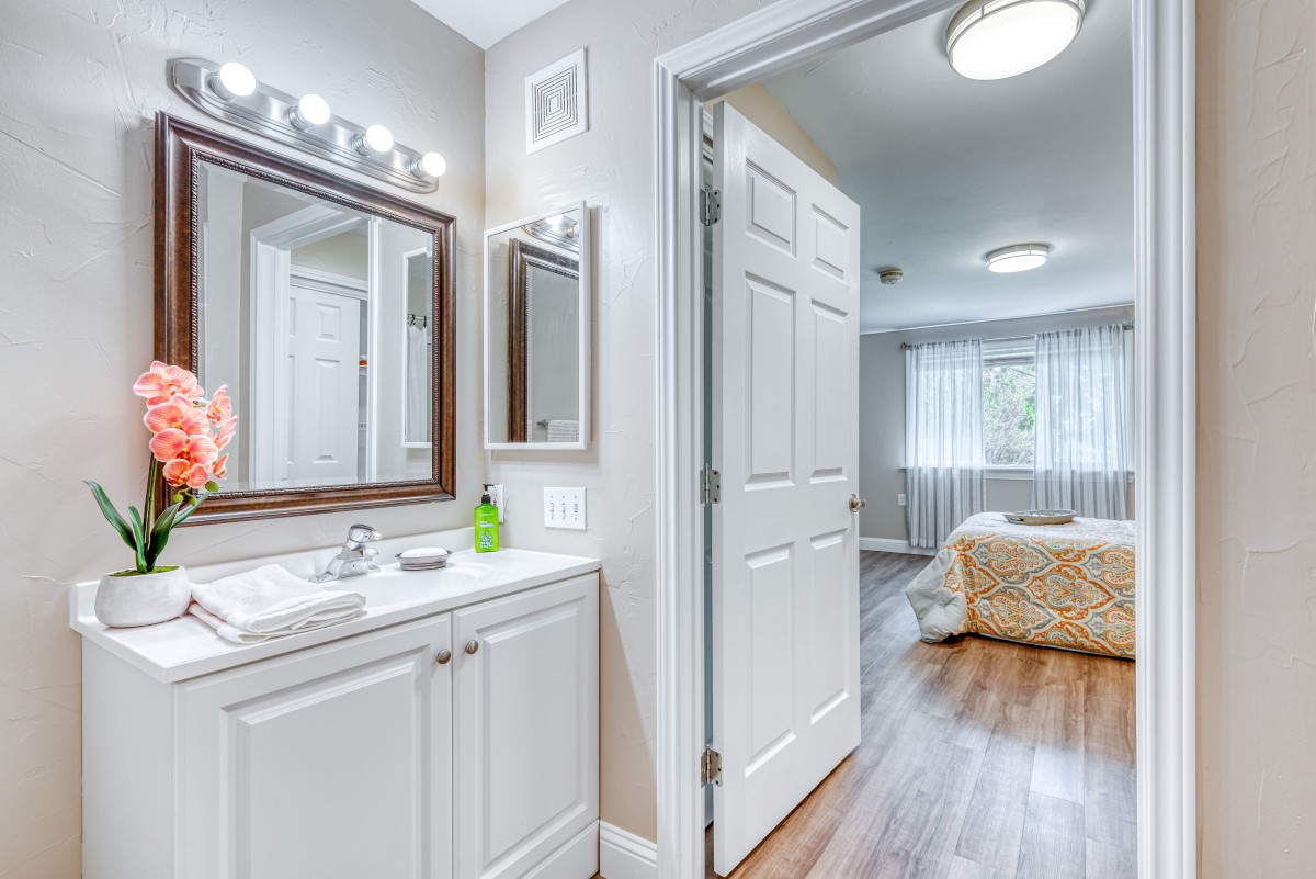A modern bathroom vanity with a view into a cozy bedroom.