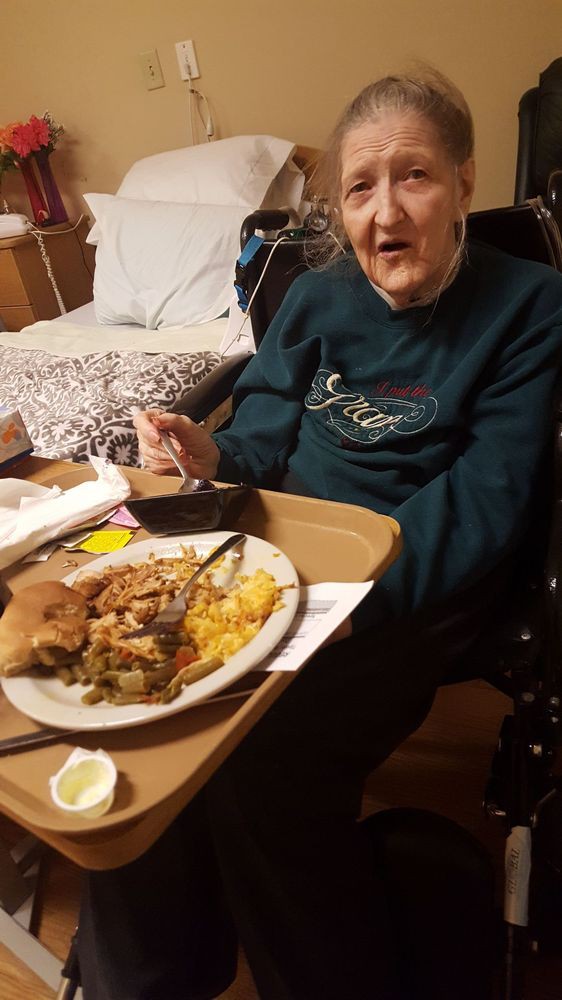 An elderly person sitting at a table with a plate of food.