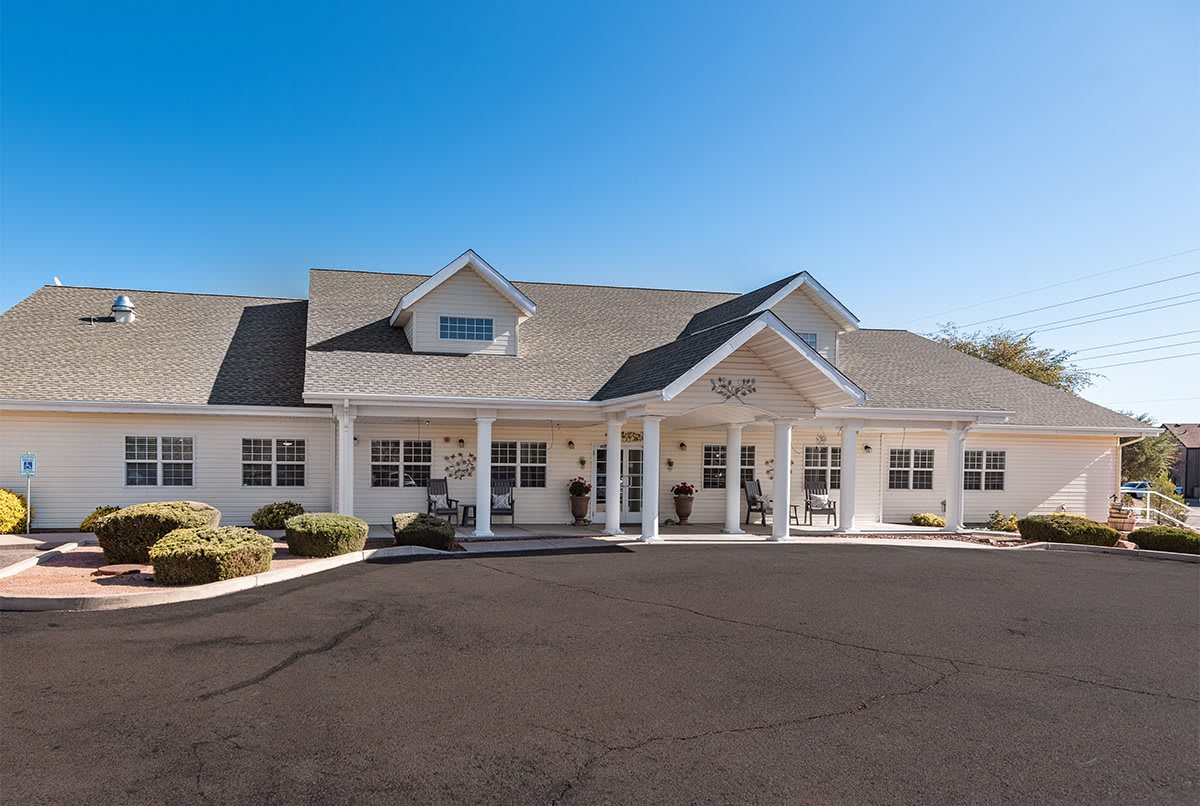 A large residential-style building with a gabled roof and a covered entrance, viewed on a sunny day.