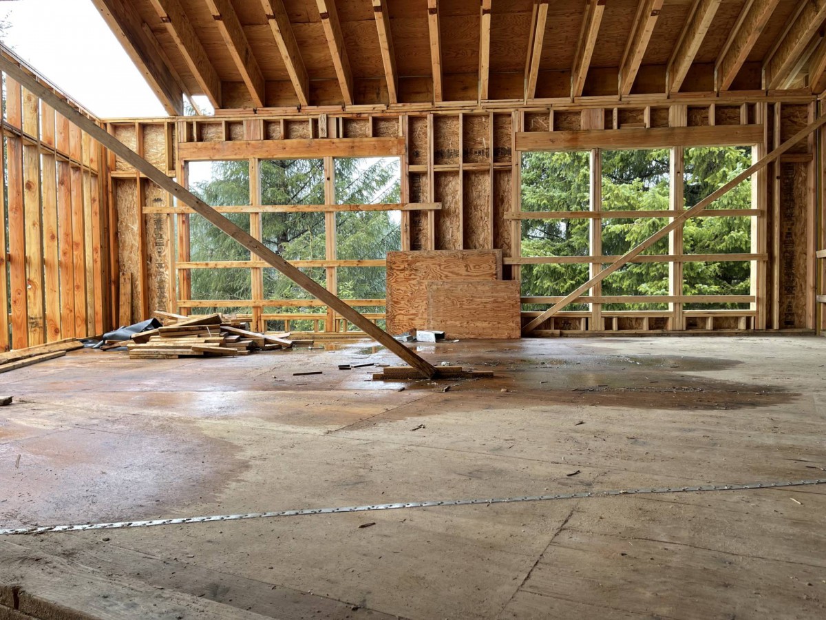 Unfinished building interior with wooden framing and large windows.