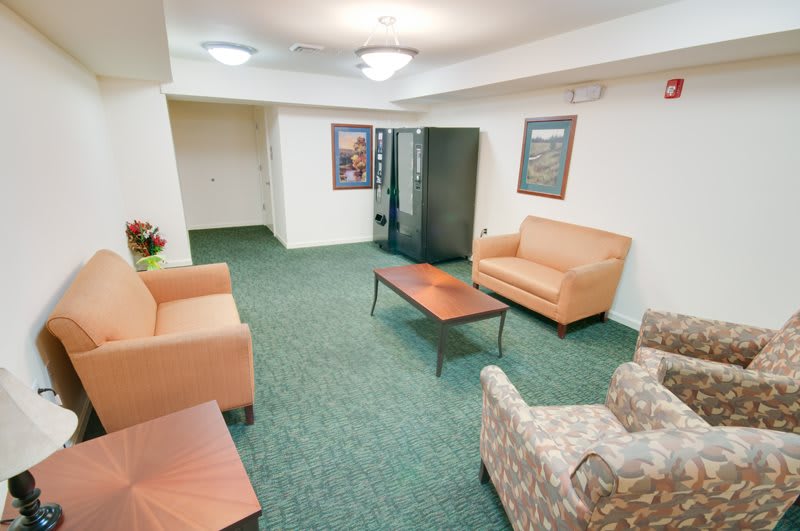 A cozy waiting area with sofas, a chair, and a vending machine.