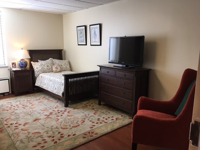 A cozy bedroom with a single bed, television, dresser, and an armchair.