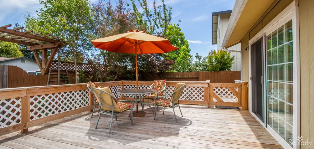 A sunny outdoor patio with a table, chairs, and an orange umbrella.
