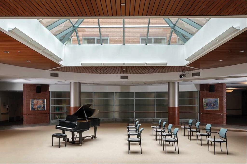 An empty concert hall with a grand piano and rows of chairs under a skylight.