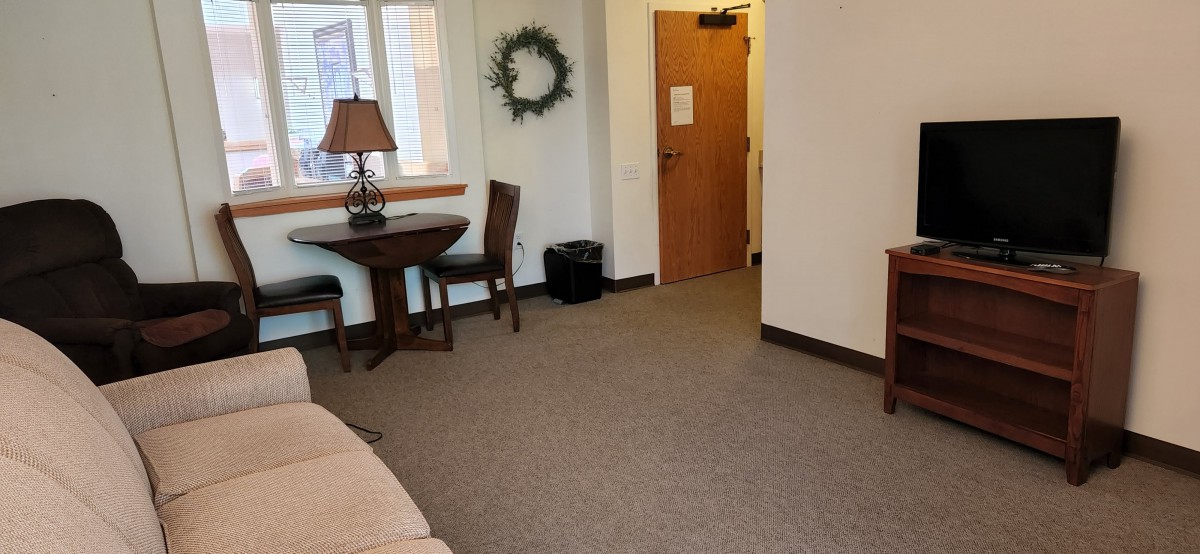 A cozy room interior with a small table, chairs, and a decorative wreath on the wall.