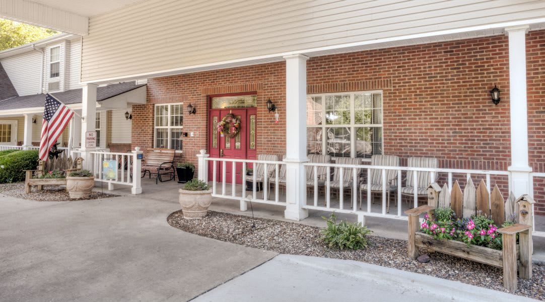 A welcoming porch with a vibrant red door, surrounded by brick walls and white railings.