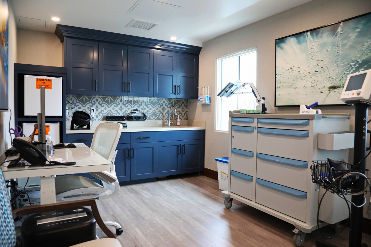 A modern clinic examination room with blue cabinetry and medical equipment.
