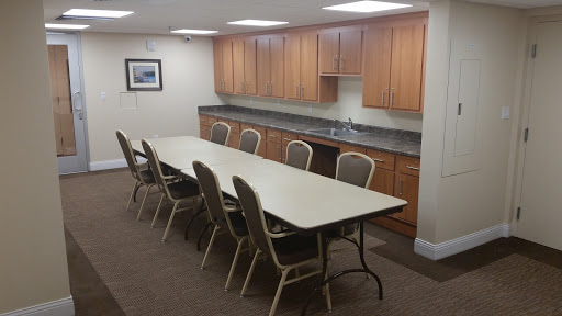 A spacious conference room featuring a long table surrounded by chairs and a kitchenette in the background.