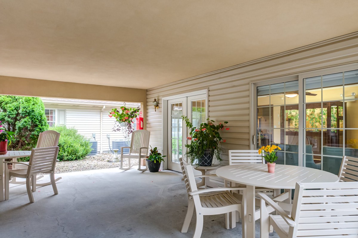 A cozy patio with a table, chairs, and vibrant plants under a sheltered area.