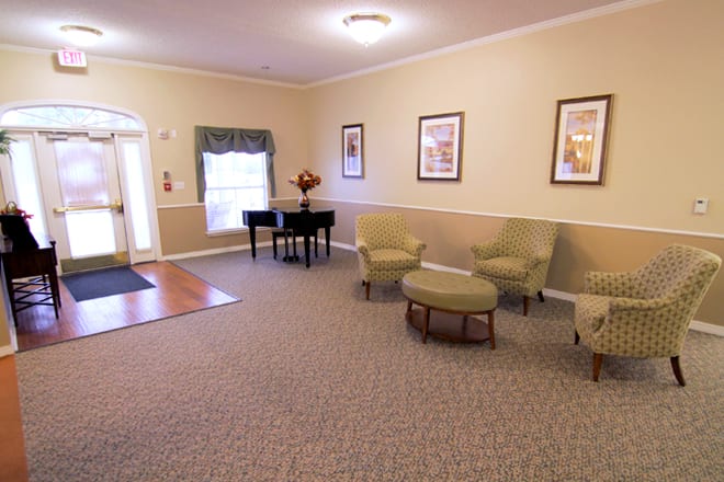 A cozy living room featuring comfortable seating, a piano, and framed artworks on the wall.