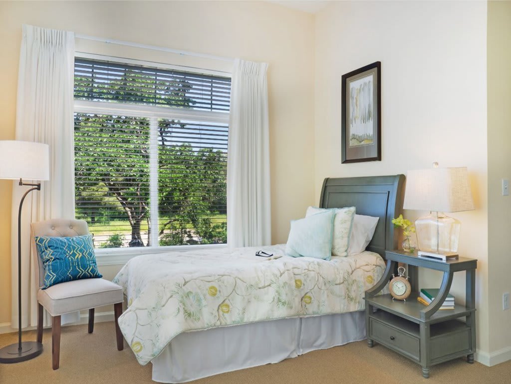 A cozy bedroom with a bed, nightstand, and large window allowing natural light to fill the room.