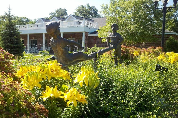 A garden scene featuring a sculpture of children playing among vibrant yellow flowers.