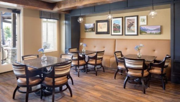 A cozy restaurant dining area with wooden tables and chairs, featuring wall art and pendant lighting.