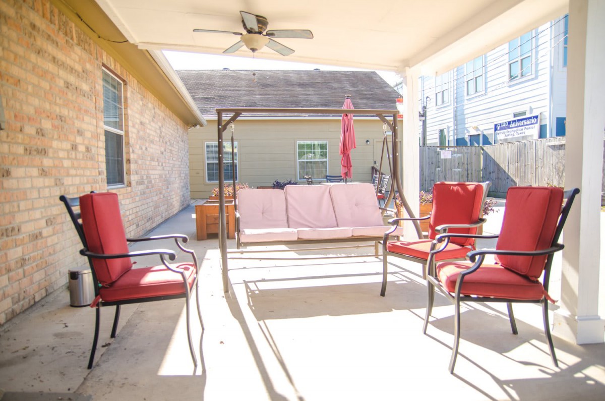 A sunny backyard patio featuring a swing chair and red cushioned seating.