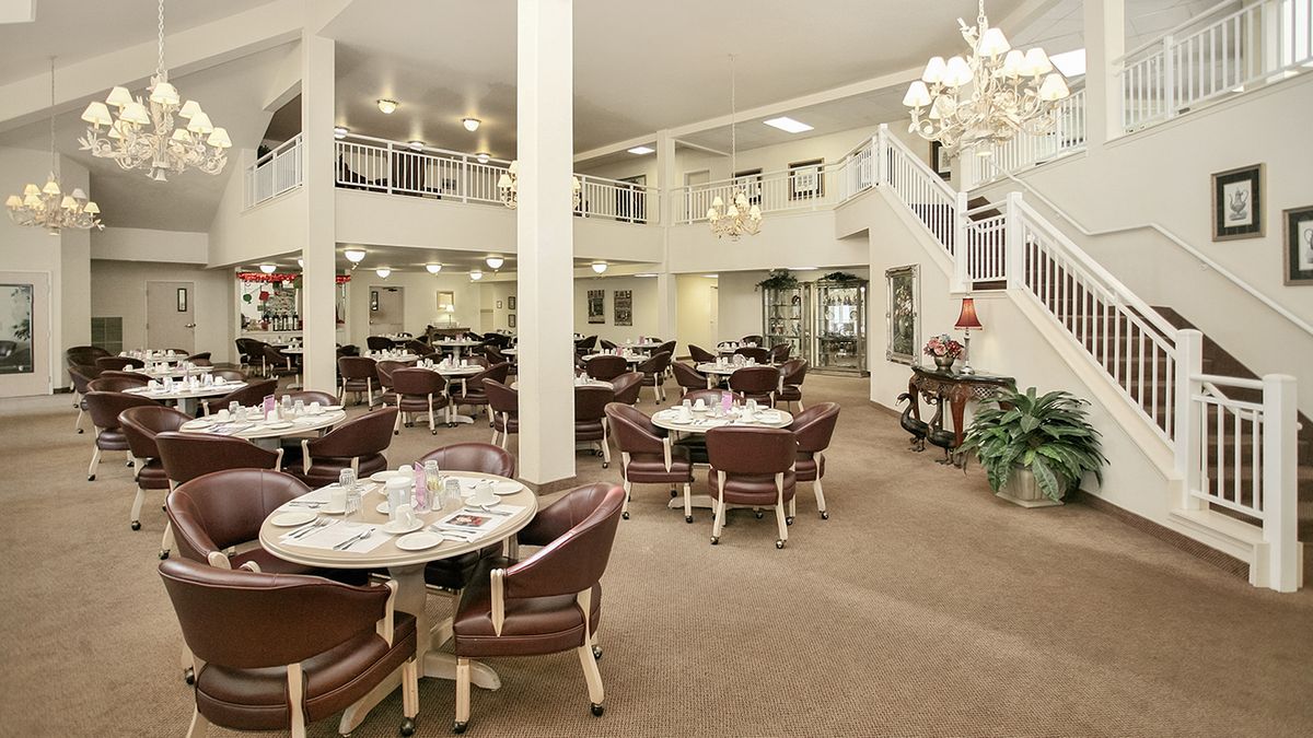 A spacious, elegant dining room with multiple round tables and chairs, featuring a two-story layout and chandeliers.