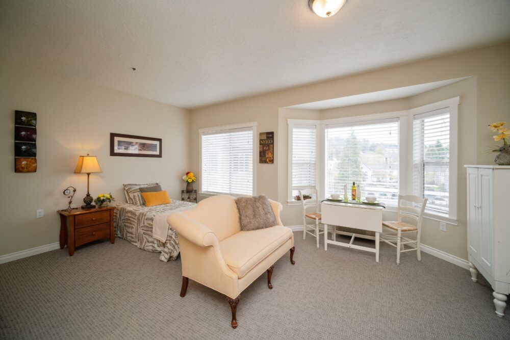 A cozy living room with a beige sofa, small table, and large windows providing plenty of natural light.