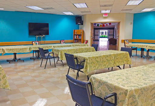 A spacious community dining area with neatly arranged tables and chairs, featuring a blue accent wall and a television.
