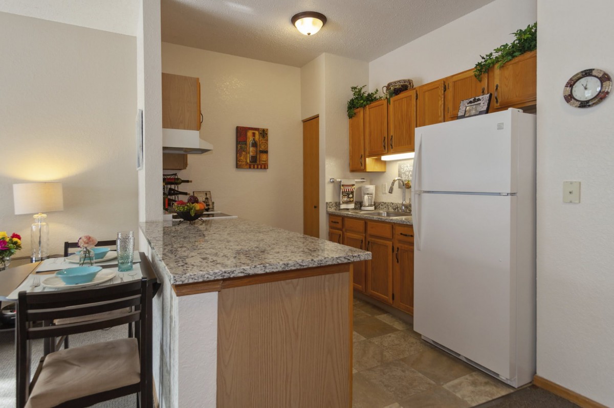 A compact kitchen with wooden cabinets, a white refrigerator, and a granite countertop.