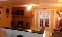 A cozy living room featuring a brick fireplace, wall-mounted TV, and French doors.