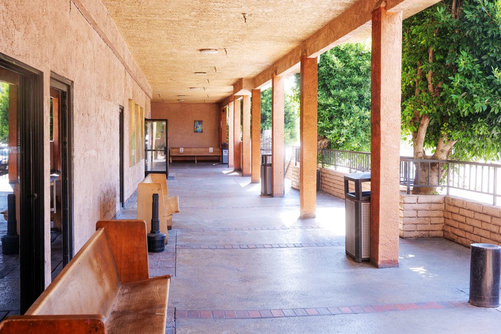 A sunlit outdoor corridor with wooden benches and columns.
