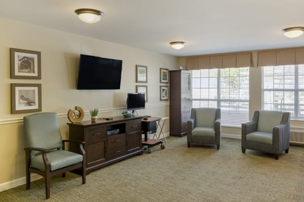 A cozy living room setting with chairs, a television, and ample natural light from a large window.