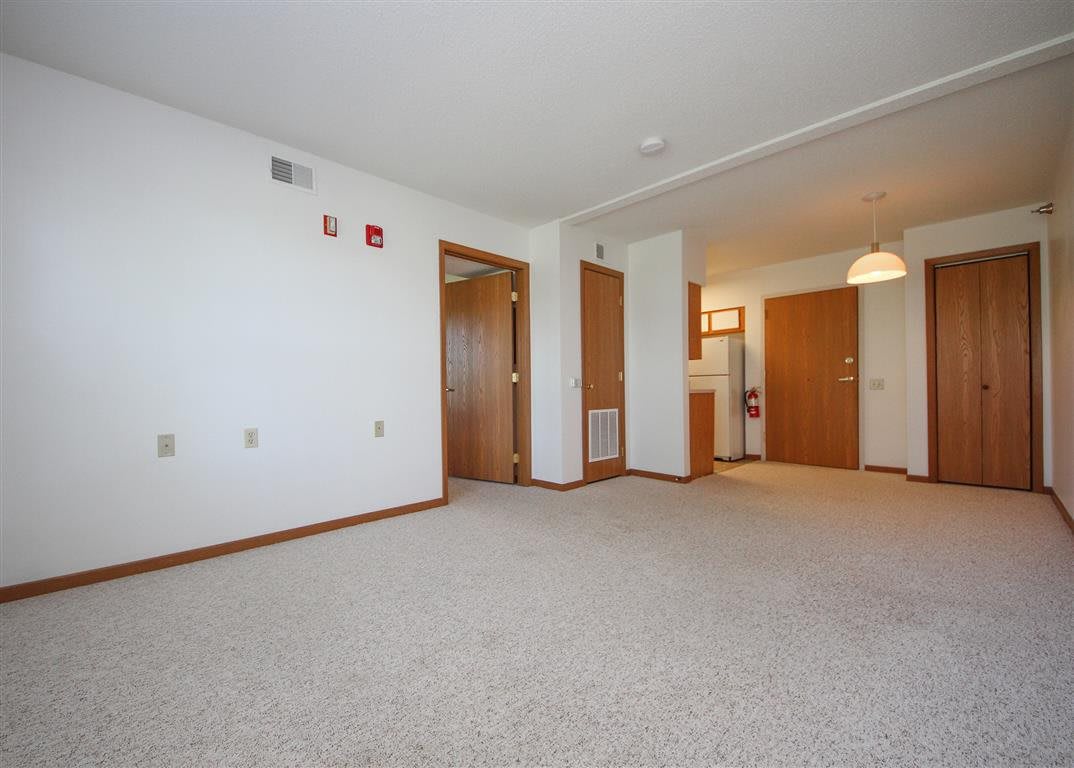A spacious, empty living room with carpeted flooring and multiple wooden doors.