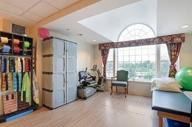 A bright exercise room with fitness equipment, a storage cabinet, and a large window.