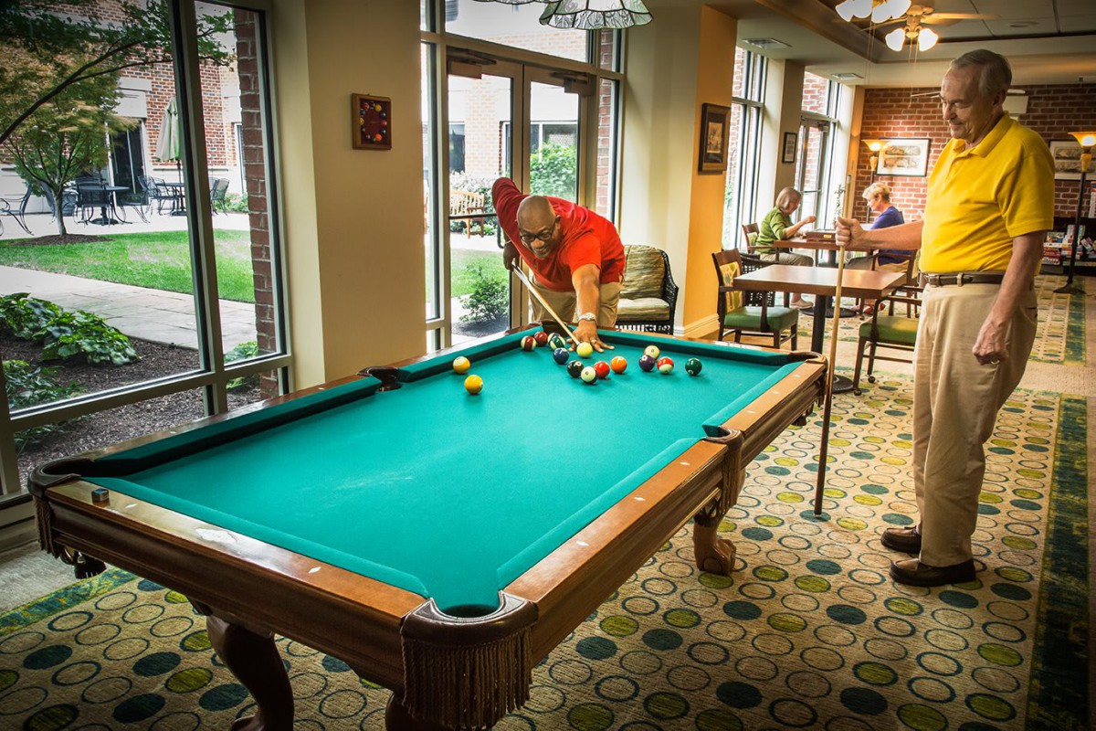 A person sets up a game of billiards on a pool table in a well-lit indoor recreational area.