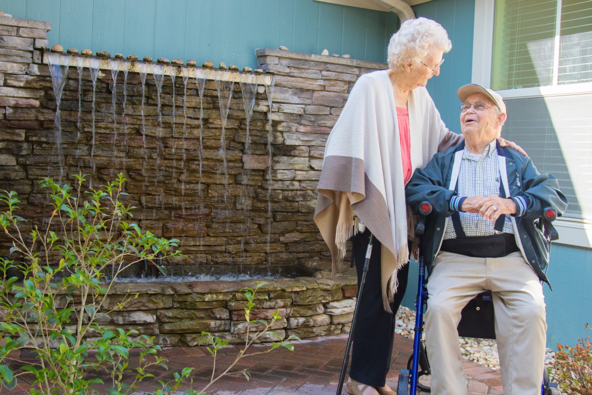 An elderly couple enjoying time together outdoors by a fountain.