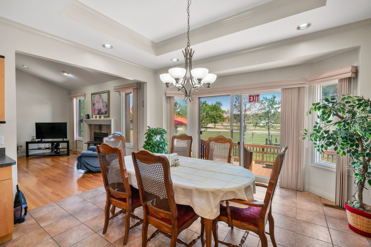 A well-lit dining room featuring a large table with chairs and a chandelier, overlooking a scenic backyard through wide sliding glass doors.