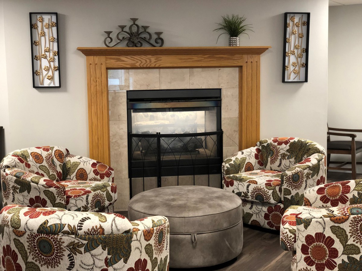 A cozy living room with a central fireplace surrounded by floral armchairs and a plush coffee table.