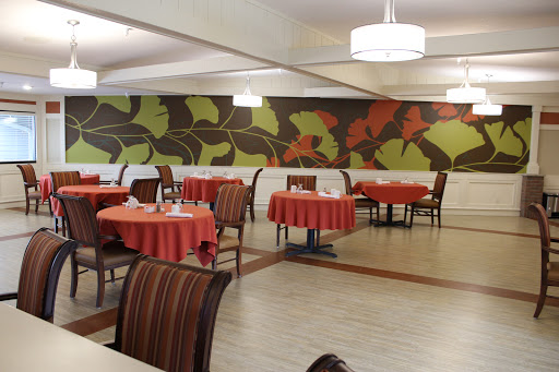 A cozy restaurant interior featuring colorful leaf patterns on the walls and tables set with red tablecloths.