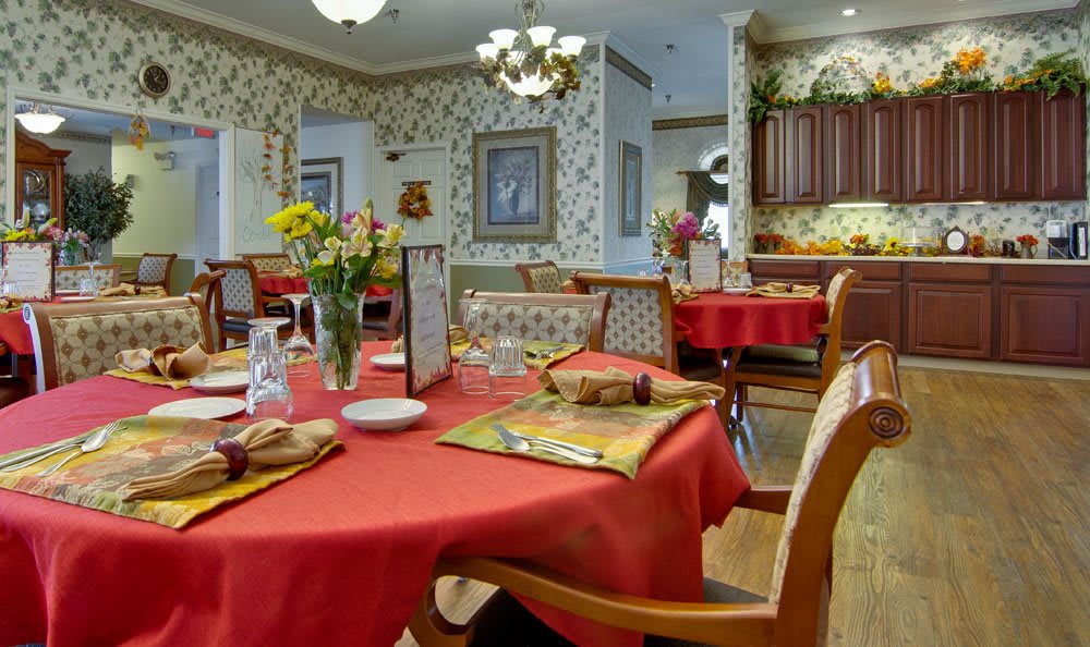 A cozy dining area with tables set for a meal, featuring colorful tablecloths and floral decorations.